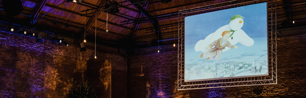 An orchestra playing music with a film screen above showing The Snowman