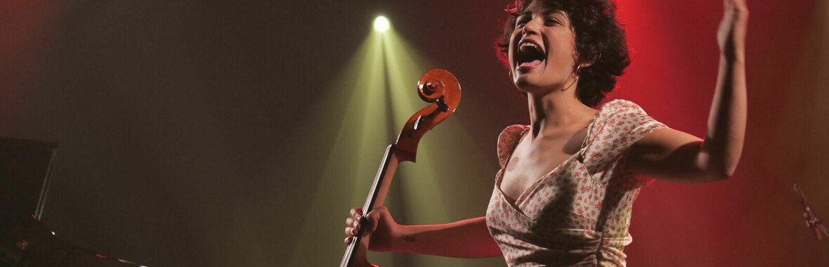Ana Carla Maza holding a cello under stage lighting