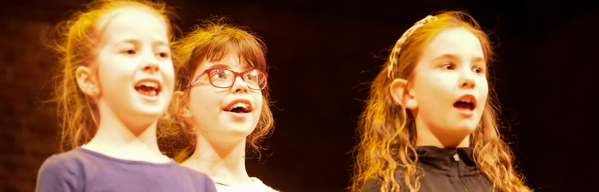 Three young people singing on stage with smiles on face